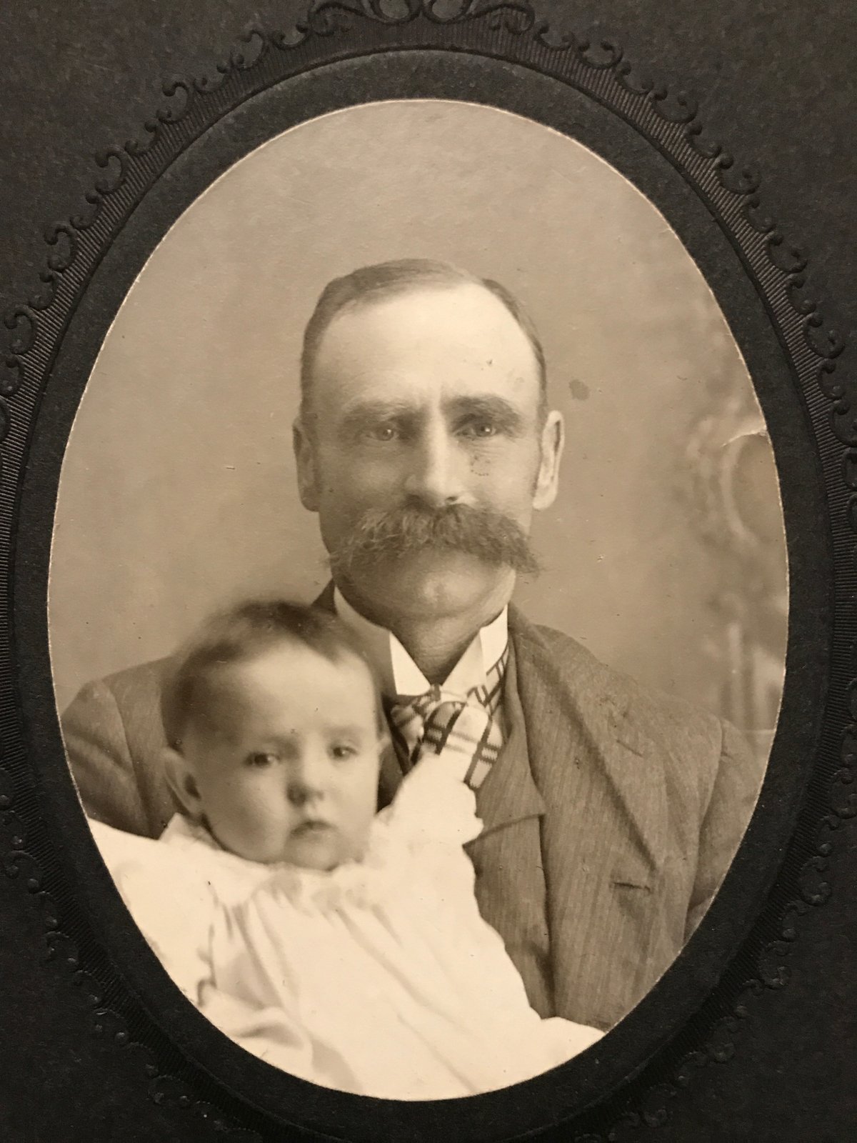 A studio portrait of a man holding an infant. The site records two possible identities for this ancestor, Jay Charles Grahm or William James Walker — it isn't known which one this photograph shows.